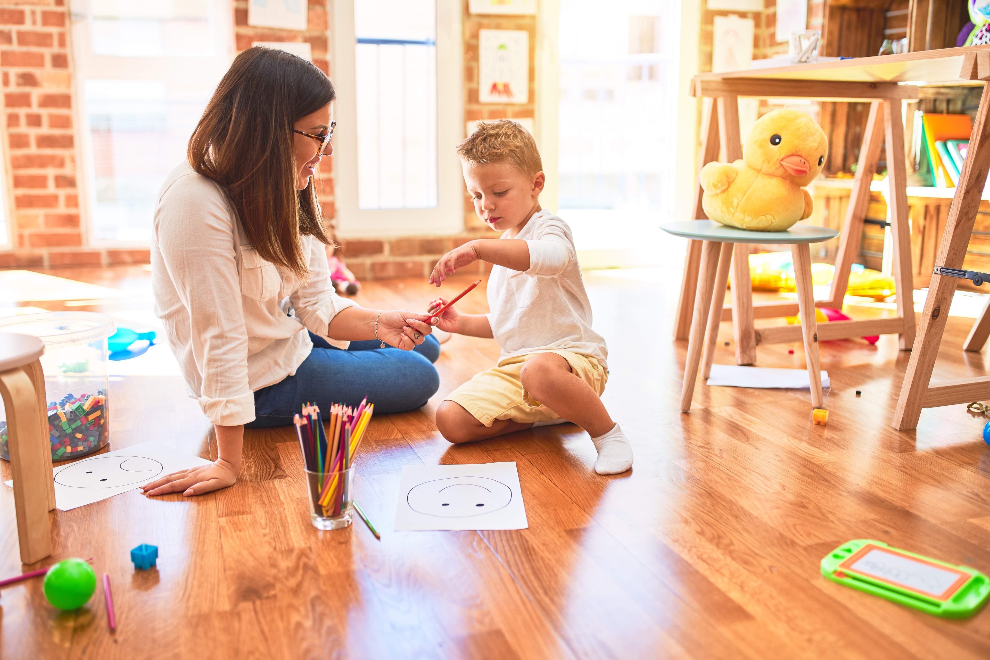 Toddler drawing with pencils surrounded by toys during ABA therapy